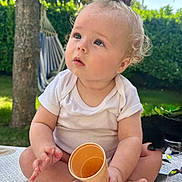 Agathe participe au concours pour gagner de l'argent avec cette photo : baby, child, outdoor, grass, tree, hammock, ice_cream_cone, curly_hair, scrunchie, sitting, white_shirt, barefoot, summer, sunlight, greenery, blanket, cute, curious, portrait, nature