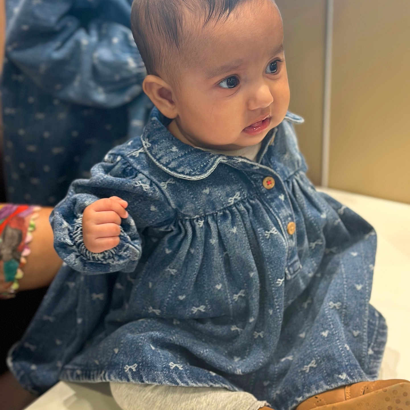 Gurrehmat is registered to the contest to win money with this photo: apparel, baby, blue, blurred_background, child, clothing, curious, cute, denim_dress, expression, face, hand, indoor, leggings, person, portrait, shoes, sitting, soft_lighting, young_child