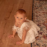 Maddy a rejoint le concours — aidez-le/la à gagner de superbes lots ! toddler, child, white_dress, crawling, wooden_floor, rug, indoor, curious, baby, person, flooring, patterned_rug, young_child, portrait, cute, elegant, feather, looking_up, small_child, home