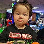 Timothy is registered to the contest to win money with this photo: child, indoor, play_area, toy_car, orange_ball, snack, black_tshirt, hair_up, cute, face, person, young_child, fun, colorful, background, lighting, expression, holding, casual, portrait