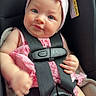 baby, child, car_seat, pink_bow, headband, pink_outfit, straps, toy, infant, cute, adorable, sitting, safety, child_safety_seat, person, closeup, face, blue_eyes, skin, indoor