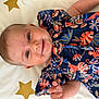 baby, smiling, child, face, blue_eyes, colorful_dress, floral_pattern, blanket, stars, infant, cute, happy, portrait, lying_down, skin, hand, young_child, soft_light, indoor, closeup