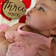 Ariella is registered to the contest to win money with this photo: baby, infant, three_months, pink_clothing, blanket, wooden_sign, face, hand, skin, cute, newborn, soft_texture, lying_down, closeup, portrait, child, young_baby, toddler, expression, colorful_background