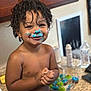 bakery, baking, blue_frosting, child, countertop, cupcakes, curly_hair, diaper, face, food, fun, happy, indoor, kitchen, messy, person, playful, smiling, sweet, toddler