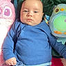 baby, blue_onesie, plush_toy, pink_toy, blue_toy, blanket, infant, lying_down, indoor, cute, child, pacifier, soft_toys, cozy, portrait, one_person, young_child, baby_clothes, face, expression