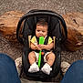 baby, car_seat, child, indoor, person, wood, carpet, footwear, jeans, toy, holding, curious, sitting, black, green, spatula, decor, floor, slippers, cute