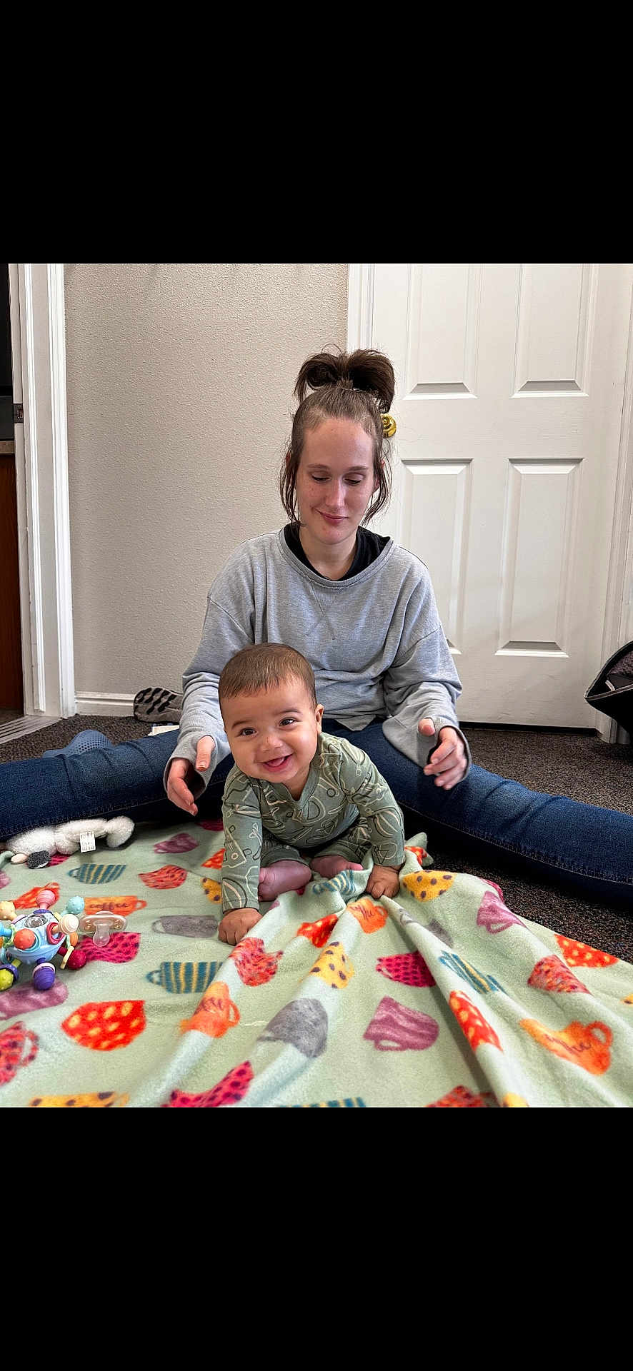 Onyx is registered to the contest to win money with this photo: baby, woman, indoor, blanket, toys, smiling_baby, casual_clothing, carpet, door, playing, child, sitting, happy, person, family, home, crawling, cute, young_child, relaxed