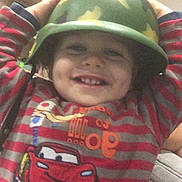 Mymy a rejoint le concours — aidez-le/la à gagner de superbes lots ! toddler, child, helmet, camouflage, striped_shirt, cartoon_car, smile, indoor, living_room, shelf, toy, happy, face, person, clothing, furniture, couch, cute, headwear, casual