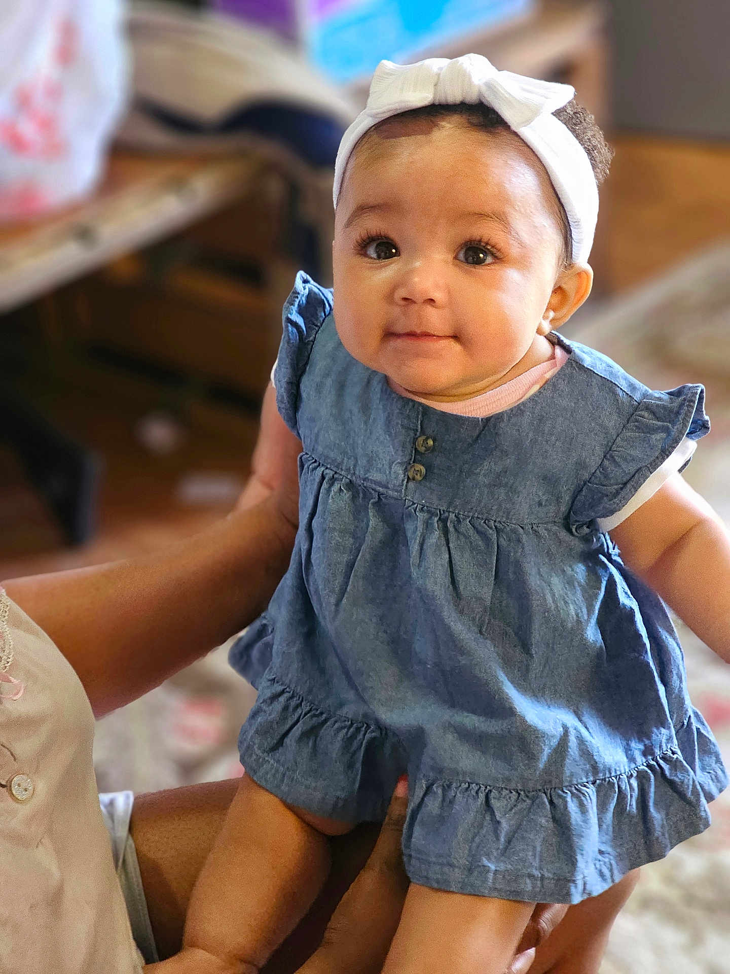 Lavinia joined the competition — help win amazing prizes! adult_hand, baby, big_eyes, blurred_background, bow, cute, denim_dress, dress, eyelashes, fabric, furniture, hands, headband, holding, indoor, infant, legs, portrait, smile, soft_lighting