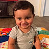 Blake is registered to the contest to win money with this photo: toddler, child, smiling, indoors, play_mat, clothing, gray_shirt, baby_wipes, toy, television, floor, face, person, happy, cute, sitting, room, hair, skin, expression