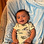 baby, infant, smiling, dinosaur_print, onesie, blanket, blue_blanket, indoor, happy, cute, child, portrait, sitting, soft_texture, wood_floor, furniture, cozy, skin, head, face
