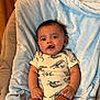 baby, infant, child, dinosaur_onesie, blue_blanket, soft_texture, indoor, cute, smiling, happy, skin, face, hands, legs, sitting, comfort, cozy, expression, portrait, young