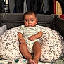 baby, infant, pillow, playpen, blanket, clothing, indoors, child, face, person, sitting, furniture, pattern, cute, young, resting, comfortable, curious, room, portrait