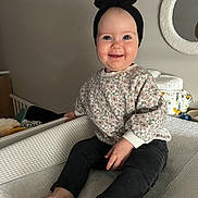 Maona a rejoint le concours — aidez-le/la à gagner de superbes lots ! baby, baby_items, barefoot, black_pants, bow, changing_table, child, cozy, cute, floral_sweater, happy, headband, home, indoor, infant, mirror, person, portrait, sitting, smiling