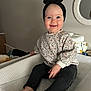 baby, baby_items, barefoot, black_pants, bow, changing_table, child, cozy, cute, floral_sweater, happy, headband, home, indoor, infant, mirror, person, portrait, sitting, smiling