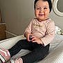 baby, black_pants, blue_object, child, cute, decor, face, footwear, happy, headband, holding_object, indoor, mirror, necklace, person, pink_shirt, pink_shoes, sitting, smiling, young_child