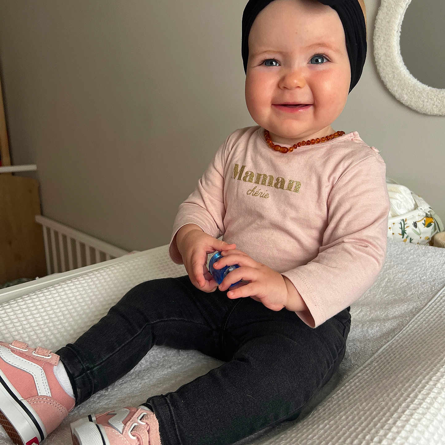 Maona participe au concours pour gagner de l'argent avec cette photo : baby, black_pants, blue_object, child, cute, decor, face, footwear, happy, headband, holding_object, indoor, mirror, necklace, person, pink_shirt, pink_shoes, sitting, smiling, young_child