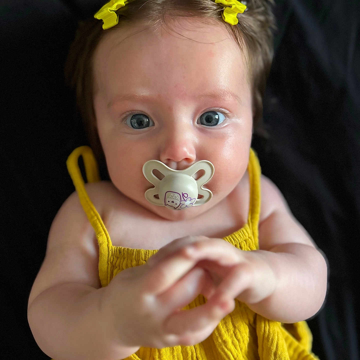 Bella-Ann joined the competition — help win amazing prizes! baby, baby_girl, background, black_background, blue_eyes, child, closeup, clothing, cute, expression, face, hands, indoors, infant, pacifier, person, portrait, skin, yellow_bows, yellow_dress