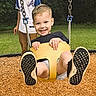 active, casual_clothing, child, daylight, feet, fun, grass, happy, joy, outdoor, park, person, play, playground, smiling, swing, trees, wood_chips, yellow_swing, young_child