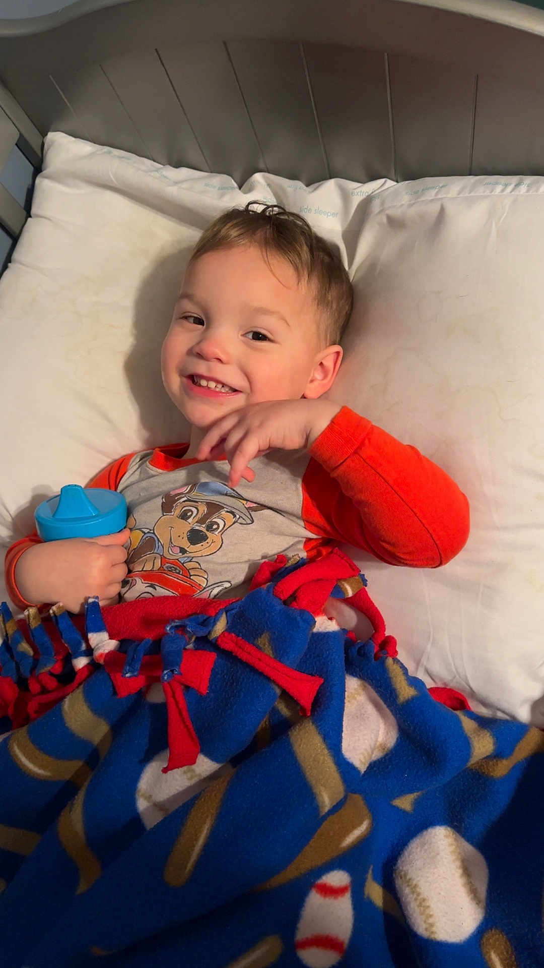 Kolton joined the competition — help win amazing prizes! child, toddler, smiling, pajamas, blanket, fleece_blanket, sippy_cup, bed, pillow, portrait, indoor, happy, face, hand, hair, lying_down, cartoon_print, headboard, cozy, closeup