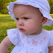 Everleigh is registered to the contest to win money with this photo: baby, cheek, child, close_up, dress, earring, embroidery, eye, floppy_hat, floral_pattern, grass, greenery, nature, outdoor, portrait, pout, serious_expression, skin, summer, sun_hat