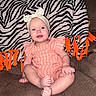Everleigh is registered to the contest to win money with this photo: baby, blanket, bow, cheeks, child, couch, eyes, feet, headband, indoor, infant, orange, portrait, romper, sitting, smiling, striped_romper, teeth, toes, zebra_blanket