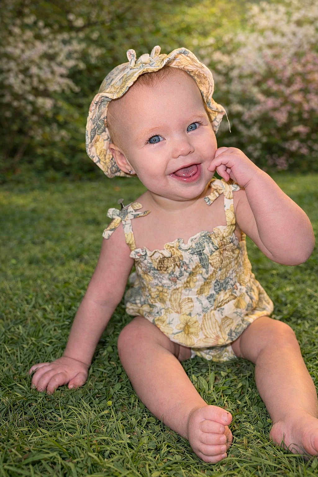Everleigh is registered to the contest to win money with this photo: baby, infant, toddler, smiling, hat, floral_outfit, grass, outdoors, portrait, blue_eyes, sitting, hand_on_face, bare_feet, earring, summer, adorable, rosy_cheeks, candid, daylight, nature