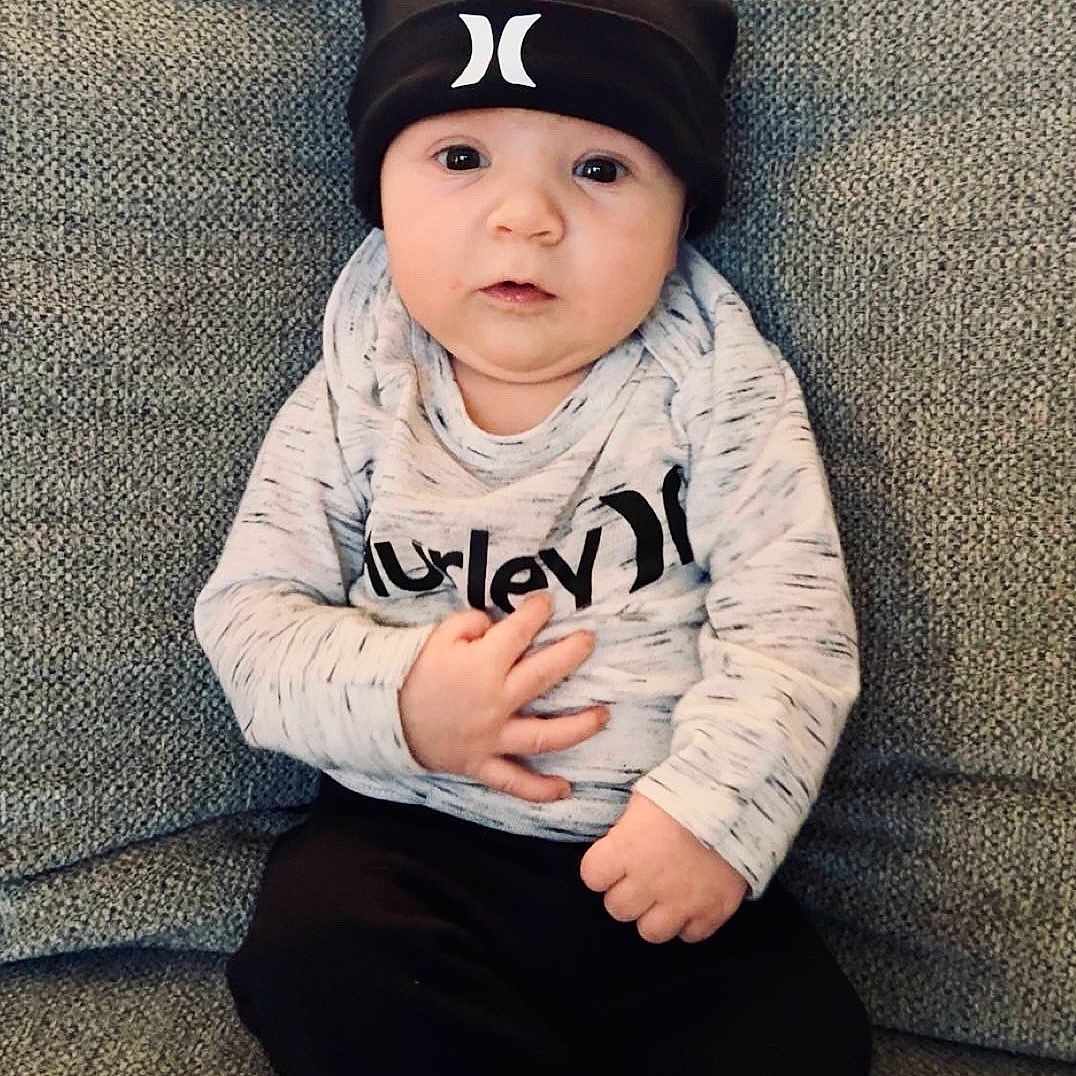 Hudson is registered to the contest to win money with this photo: baby, baseballcap, cap, clothing, couch, cushion, face, furniture, hat, head, homedecor, longsleeve, pants, people, person, photography, portrait, sitting, sleeve, t_shirt