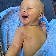 Charlie is registered to the contest to win money with this photo: baby, infant, smiling, laughing, blue_blanket, soft_texture, skin, face, closed_eyes, happy, lying_down, couch, arm, hand, newborn, cute, indoors, person, child, portrait