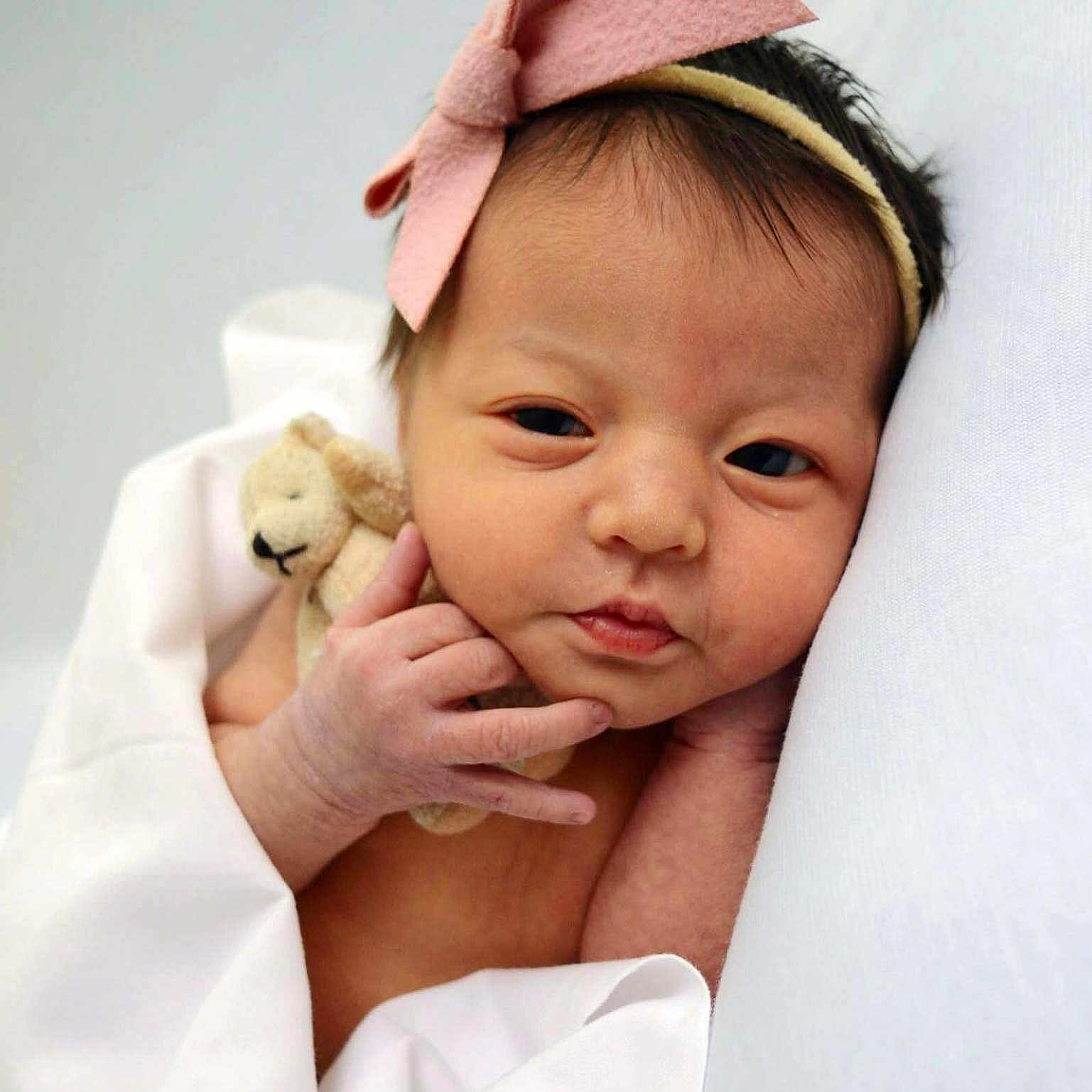 Abigail is registered to the contest to win money with this photo: baby, blanket, child, cute, face, hand, headband, indoors, infant, newborn, person, pink_bow, portrait, resting, skin, sleeping_area, small, soft, teddy_bear, wrapped