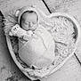 newborn, baby, sleeping, wrapped, knit_hat, plush_toy, heart_shaped_bowl, blanket, cozy, black_and_white, portrait, infant, cute, peaceful, soft_texture, child, resting, small_hands, adorable, studio_photo