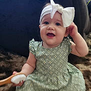 Ava joined the competition — help win amazing prizes! baby, child, girl, headband, bow, green_dress, sitting, brush, furry_surface, happy, cute, indoor, portrait, infant, smiling, hand, face, person, clothing, head