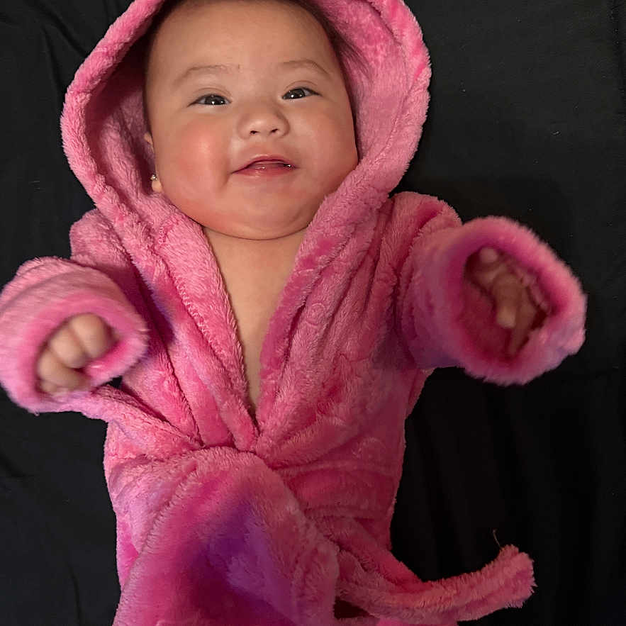 Valeria Rose is registered to the contest to win money with this photo: adorable, baby, baby_clothing, blanket, cheeks, cheerful, child, cozy, cute, eyes, hand, hood, indoor, infant, lying_down, pink_robe, portrait, skin, smile, soft_texture