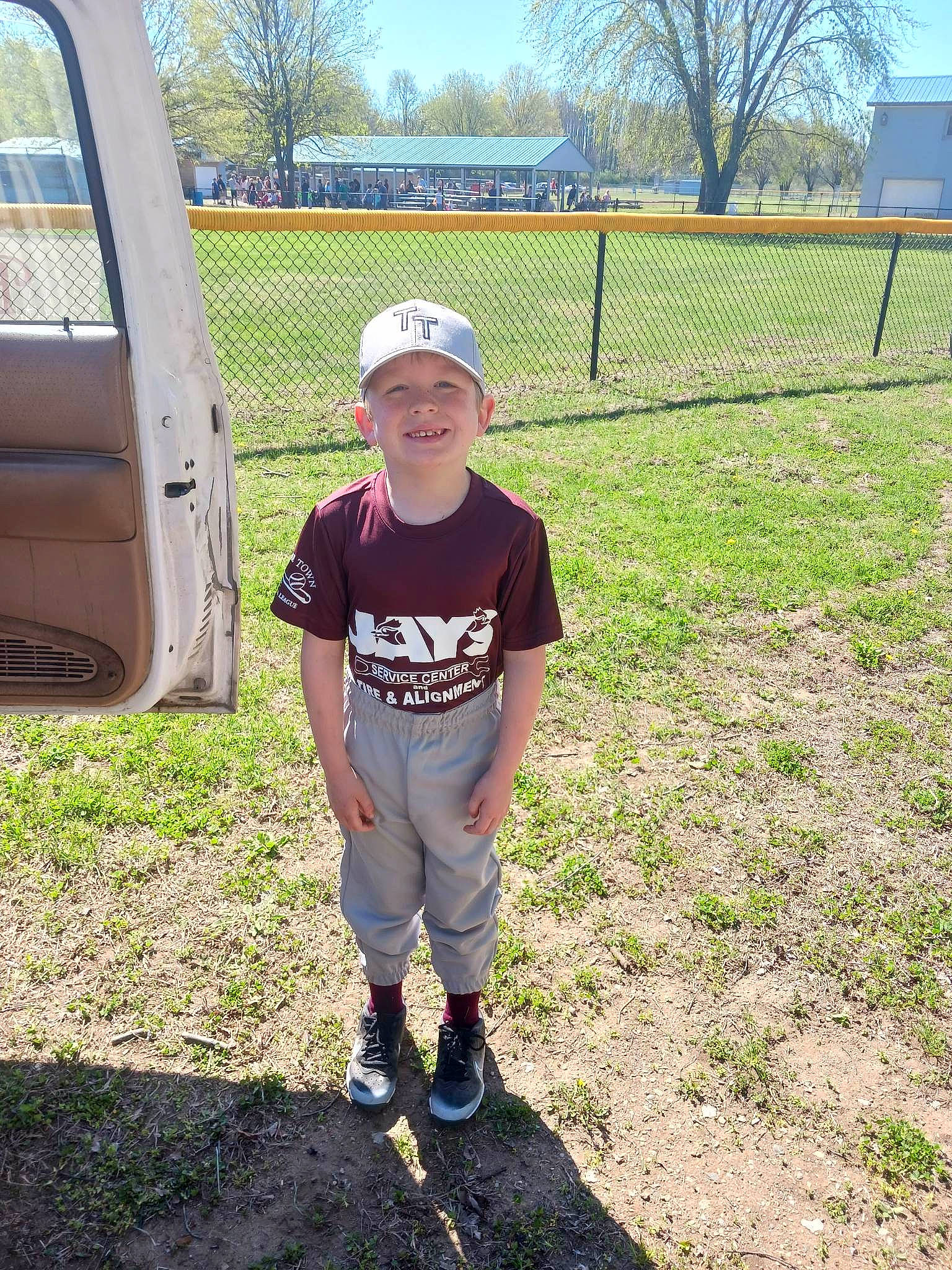 Malachi is registered to the contest to win money with this photo: automotive_exterior, baseball_cap, cap, fence, fun, grass, grassland, hat, headwear, joy, lawn, leisure, person, plant, player, recreation, sky, smile, soil, t_shirt