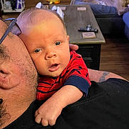 Wyatt joined the competition — help win amazing prizes! baby, adult, dog, couch, living_room, table, remote_control, toy, person, clothing, face, hand, glasses, tattoo, floor, furniture, home_interior, carpet, comfort, relaxation