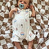 baby, infant, blanket, onesie, pacifier, face, foot, hand, lying_down, pattern, brown, white, clothing, person, cute, sleepwear, newborn, indoors, soft, comfort
