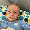 Crew is registered to the contest to win money with this photo: baby, smile, infant, pillow, fish_pattern, blanket, blue_clothing, couch, indoor, face, head, person, child, happy, cute, portrait, cozy, resting, expression, skin