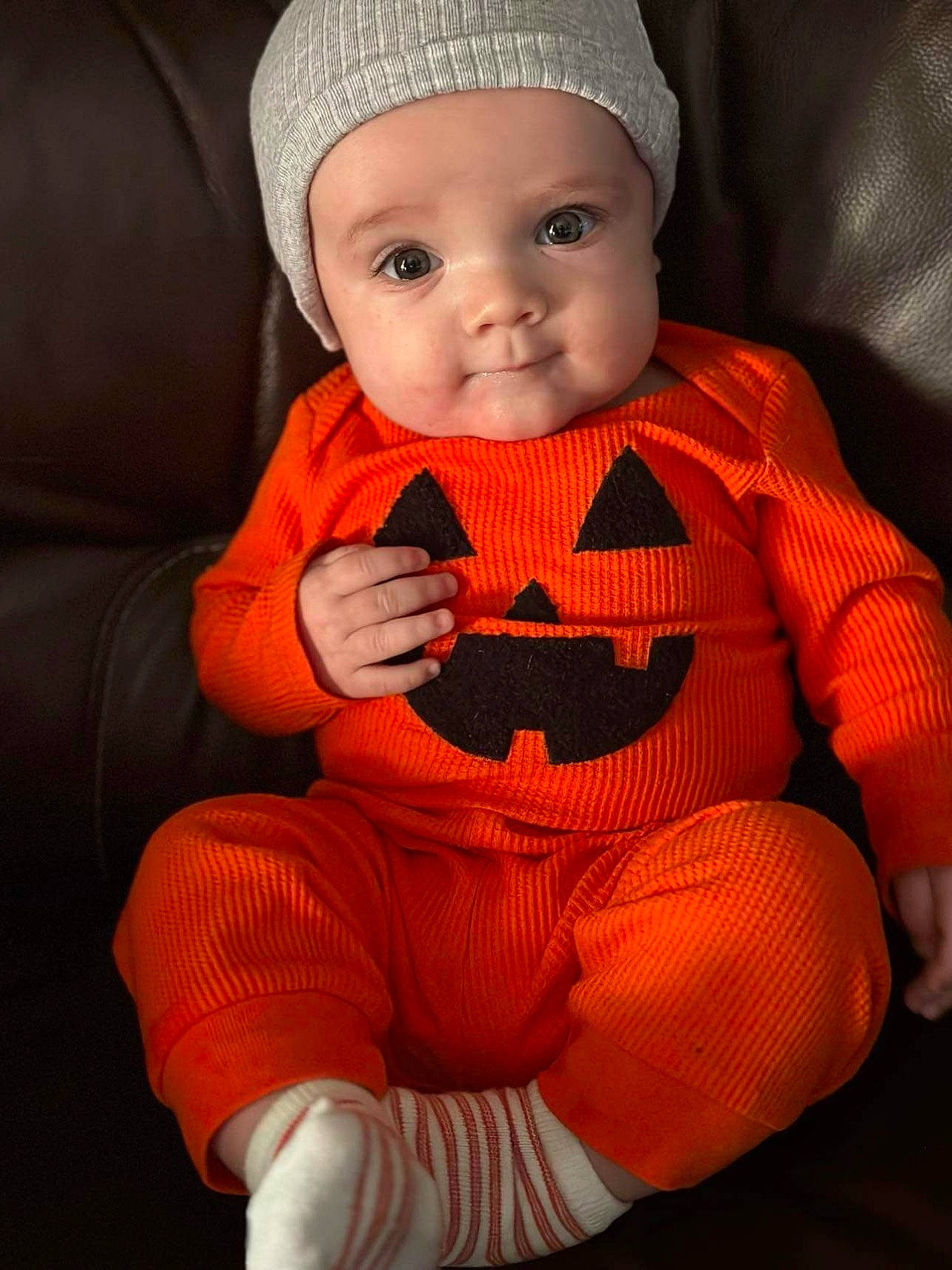 Everett is registered to the contest to win money with this photo: arm, baby, baby_toddler_clothing, cap, cheek, child, comfort, dress, eye, face, finger, hand, headgear, headwear, lip, neck, orange, outerwear, person, skin