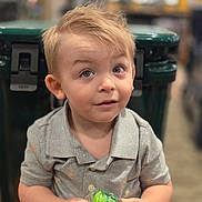 Declan joined the competition — help win amazing prizes! toddler, child, baby, boy, portrait, face, smiling, curious, blond_hair, blue_eyes, sitting, shirt, gray_clothing, toy, green_toy, packaging, indoors, store, blurred_background, photography