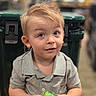 toddler, child, baby, boy, portrait, face, smiling, curious, blond_hair, blue_eyes, sitting, shirt, gray_clothing, toy, green_toy, packaging, indoors, store, blurred_background, photography