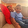 child, toddler, smiling, sleepy, couch, red_pillow, hand_holding, blue_shirt, denim_jeans, indoor, home, kitchen, family, happy, relaxed, sitting, person, furniture, portrait, cute
