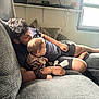 baby, child, man, couch, living_room, window, light, pillow, relaxing, casual_clothing, home, indoor, family, comfort, sitting, person, curtains, bracelet, shorts, hair