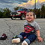 toddler, child, toy_cars, red_truck, parking_lot, asphalt, cloudy_sky, trees, casual_clothing, socks, bracelet, happy, smiling, outdoor, vehicle, nature, playful, jeans, street_lamp, daylight