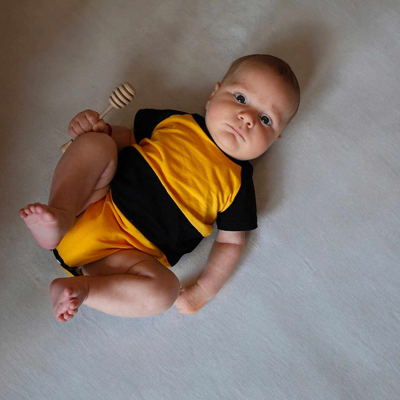 Matei joined the competition — help win amazing prizes! baby, barefoot, black_clothing, casual, child, cute, expression, honey_dipper, human, indoors, infant, looking_up, lying_down, one_person, portrait, skin, soft_surface, wooden_toy, yellow_clothing, young_child