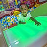 child, indoor, playground, ball_pit, slide, colorful, green_light, pigtails, curious, play, fun, young, person, smile, toy, entertainment, recreation, happy, leisure, casual
