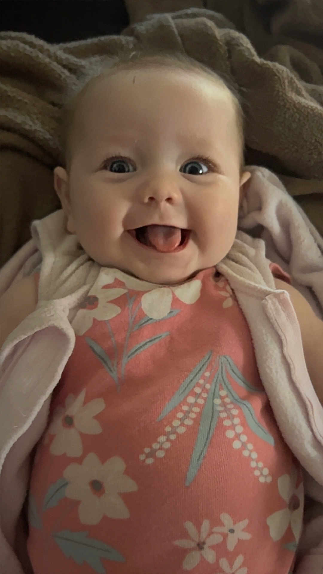 Remi is registered to the contest to win money with this photo: baby, infant, smiling, tongue_out, face, eyes, clothing, floral_pattern, blanket, cozy, cute, happy, portrait, child, indoors, soft_lighting, apparel, person, young, head