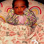 baby, infant, blanket, floral_pattern, pillow, rainbow_pattern, face, cute, soft, cozy, clothing, lying_down, indoors, patterned, person, newborn, child, portrait, warm, resting