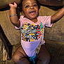baby, child, infant, smiling, happy, onesie, bracelet, pacifier, bow, couch, furniture, indoor, person, cute, skin, expression, relaxing, sitting, clothing, home