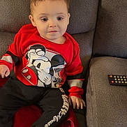Gunnar joined the competition — help win amazing prizes! toddler, child, sitting, couch, red_blanket, remote_control, coca_cola_can, mickey_mouse, clothing, socks, indoors, casual, curious, face, person, furniture, relaxed, young_child, home, soft_lighting