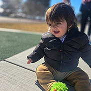 Royal joined the competition — help win amazing prizes! blurred_background, casual_clothing, child, cute, daylight, fun, green_slippers, happy, jacket, nature, outdoor, park, person, playful, sidewalk, sitting, smiling, sunny, toddler, winter_wear